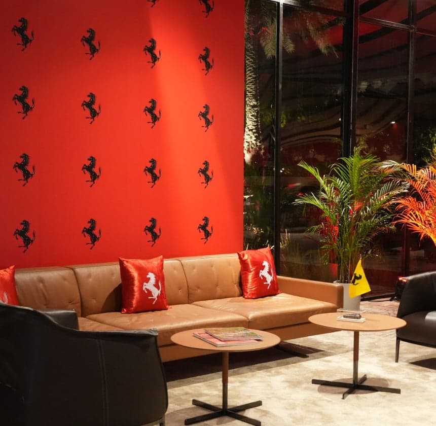 A Ferrari Pavilion lounge: a tan leather sofa with prancing-horse cushions against a red wall of black Ferrari horses